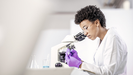 Wetenschapper in een laboratoriumjas onderzoekt een monster onder een microscoop, met focus en precisie.