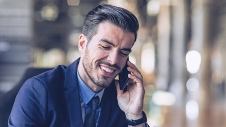 Zakelijke professional in een pak lacht tijdens een telefoongesprek, zittend in een moderne kantooromgeving.