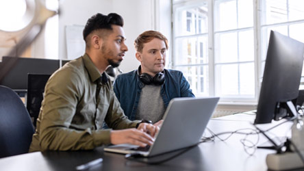 two men sitting at a table working on a laptop