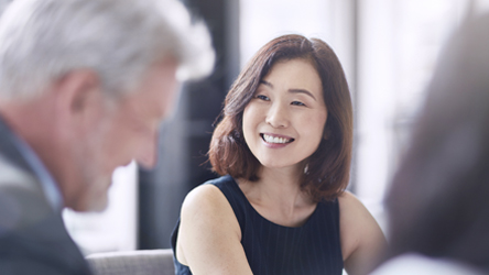 Vrouw glimlacht tijdens een zakelijke bijeenkomst, terwijl ze in gesprek is met collega's.