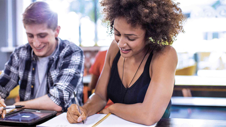 Twee studenten, een man en een vrouw, werken samen aan een opdracht in een klaslokaal, lachend en geconcentreerd.