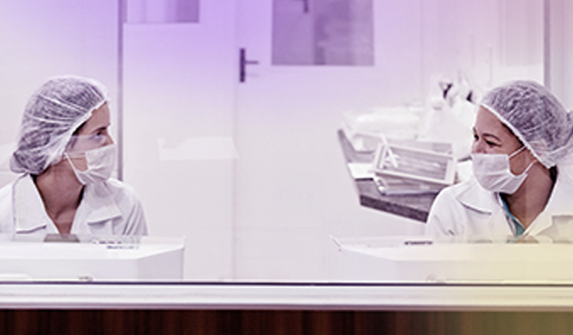 Twee laboratoriummedewerkers in beschermende kleding kijken elkaar aan in een steriele laboratoriumomgeving