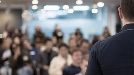 A man standing and speaking to a room of interested people 