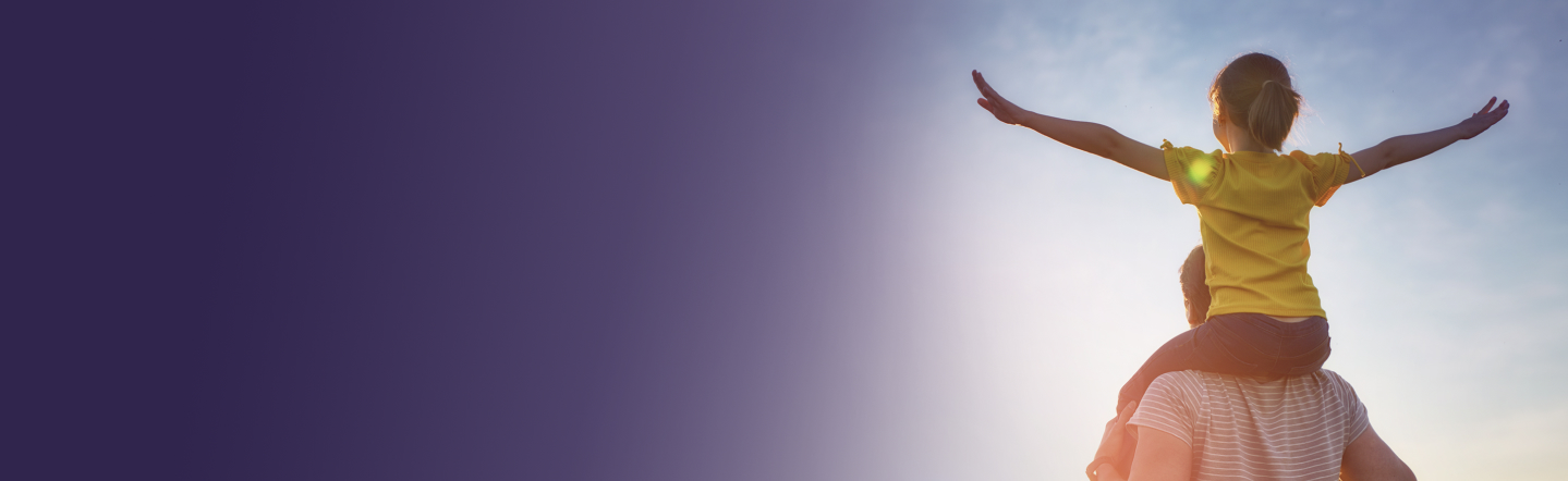 Un enfant sur les épaules d'un adulte, les bras écartés face à un ciel clair.